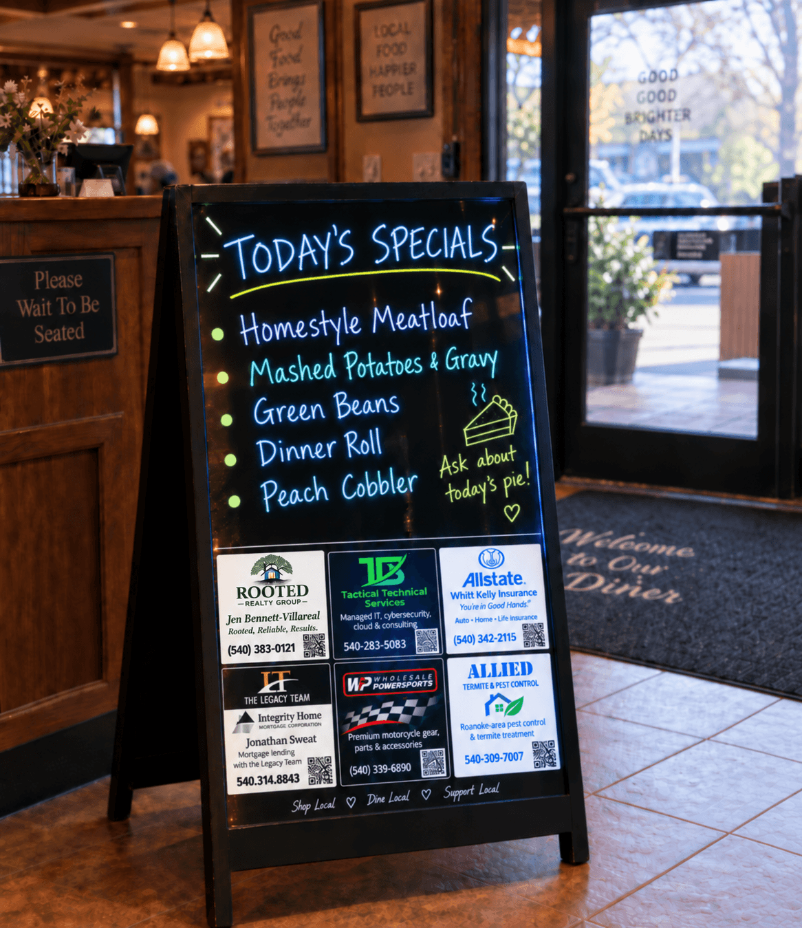 An illuminated black A-frame specials board at a restaurant entrance, with handwritten daily specials above six advertisements